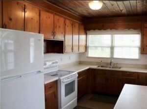 Wooden ceiling with a wooden cabinets, a fridge, a stove, and a sink with cleared out counters.